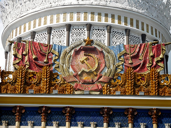 Павильон 58 на ВДНХ: герб Украины над центральным входом в обрамлении знамен
